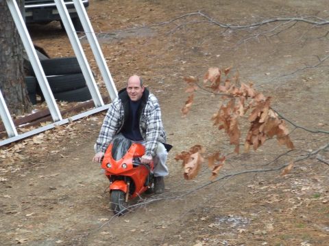 1978 Ford F-250 - A man rides an orange mini motorcycle on a dirt path, with trees and branches in the background.