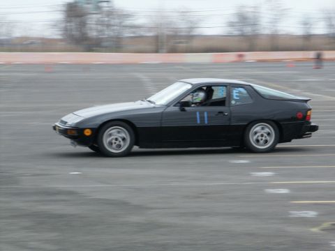 2001 Mercury Grand Marquis - A black coupe with racing numbers is captured in motion on a track, with a driver visible inside.