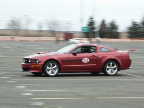 2001 Mercury Grand Marquis - A red coupe, likely a Ford Mustang, is seen in motion on a race track with orange cones visible.