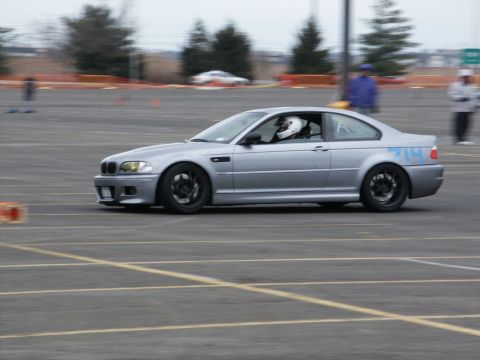 2001 Mercury Grand Marquis - A silver coupe with racing number 714 is captured in motion during a track event, with a driver wearing a helmet visible inside.