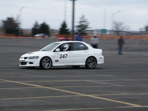 2001 Mercury Grand Marquis - A white Mitsubishi Lancer Evolution with racing decals is captured in motion on a track, with a driver in a helmet visible.