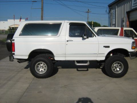 1993 Ford Bronco - White Ford Bronco, lifted, side view. Another vehicle partially visible behind it.