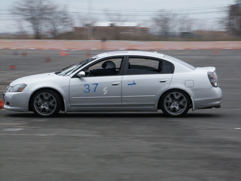 2001 Mercury Grand Marquis - A silver sedan with racing numbers is captured in motion on a race track.