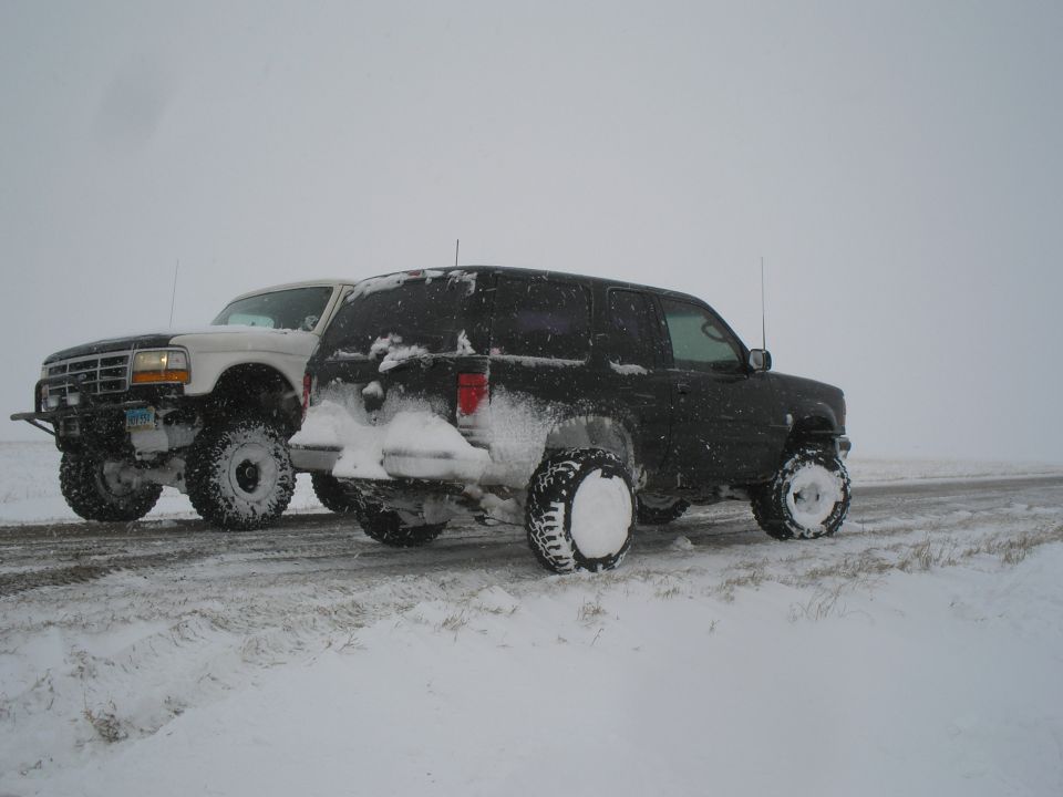 White Ford F-150 pickup truck and a black SUV parked on a snowy road
