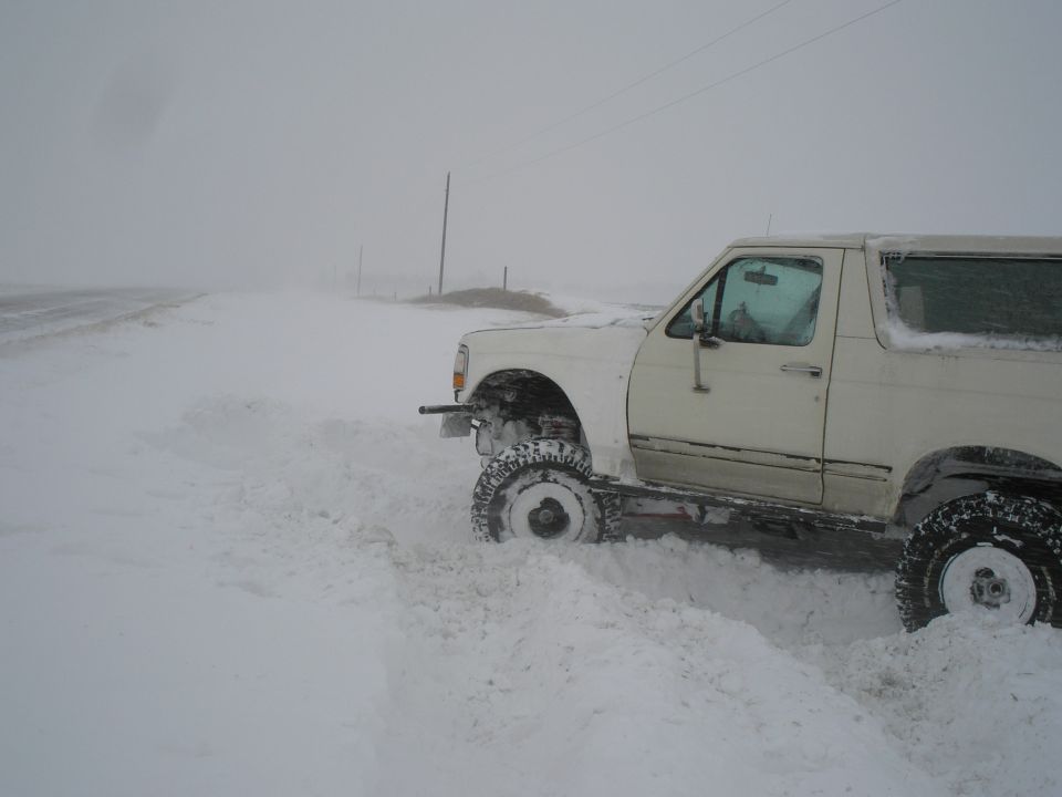 White 1990 Ford Bronco stuck in deep snow on a rural road during a blizzard