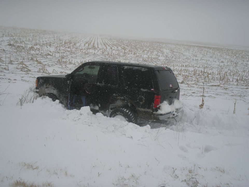 Black SUV stuck in deep snow in a field with corn stalks