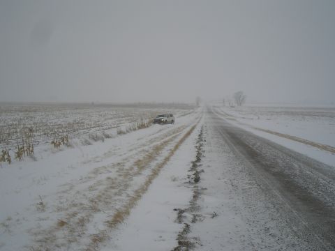 1990 Ford Bronco - A white SUV is partially off the road on a snow-covered rural route.