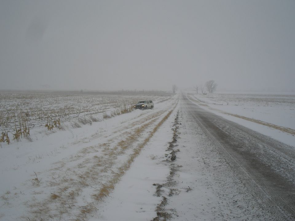 White SUV stuck on a snowy road with fields on either side
