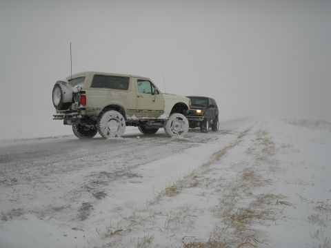 1990 Ford Bronco - Two SUVs navigate a snowy road during a winter day.