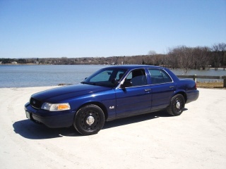 2003 Ford Crown Victoria - A blue 2003 Ford Crown Victoria sedan is parked outdoors near a waterfront on a clear day.