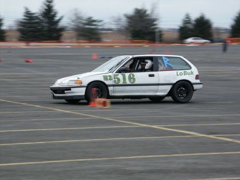 2001 Mercury Grand Marquis - A white hatchback race car with the number 516 and 'Lo Buk' visible on its side navigates a cone course on a paved track.