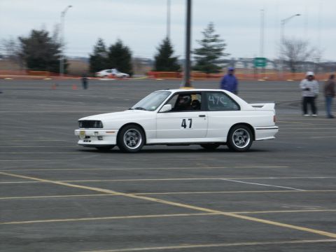 2001 Mercury Grand Marquis - A white BMW E30 coupe is seen on a race track with racing numbers displayed on its doors and windows.