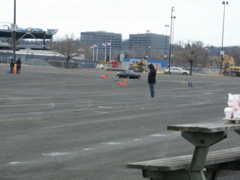 2001 Mercury Grand Marquis - A person stands near a black convertible sports car in a large paved lot marked with cones.