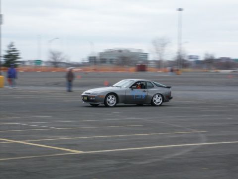 2001 Mercury Grand Marquis - A gray Porsche 944 is seen drifting on a paved lot with orange cones in the background.