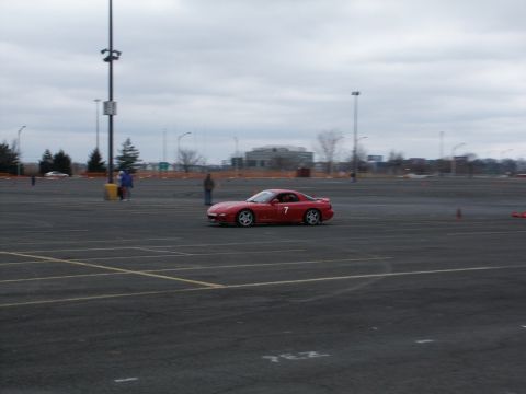 2001 Mercury Grand Marquis - A red sports car is driven in a large parking lot, possibly during an event.