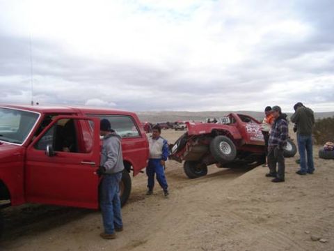 1984 Ford Bronco - Two vehicles are in a sandy area, one appears stuck while people gather around.