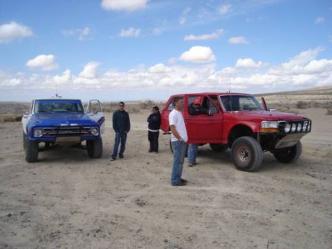 1984 Ford Bronco - A red Ford Bronco, likely from the early to mid-1990s, is parked in a desert landscape next to a blue pickup truck.