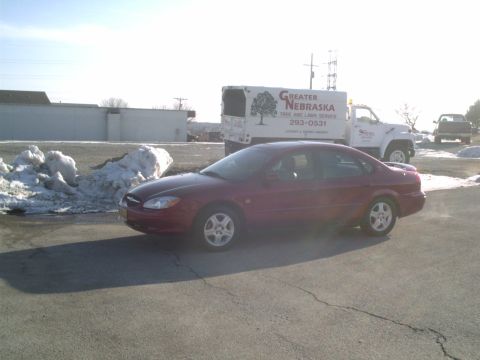 2000 Ford Taurus - A red sedan is parked next to snow piles, with a service truck in the background.