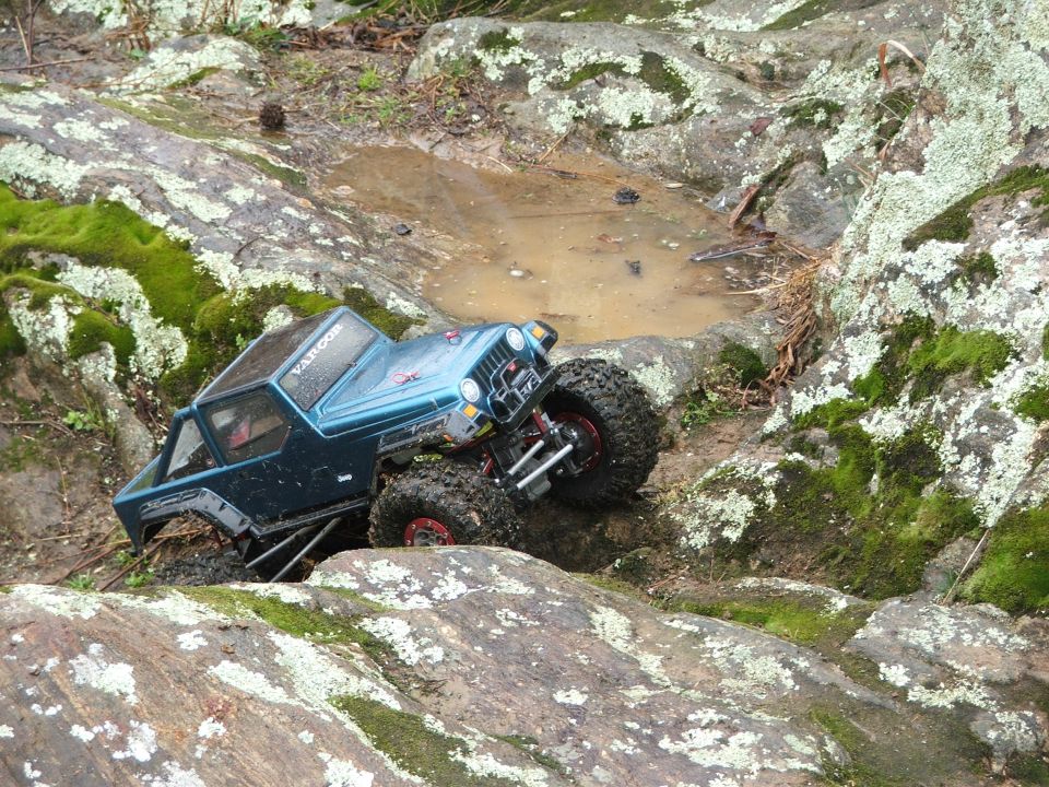 Blue off-road RC car navigating rocky terrain near a puddle