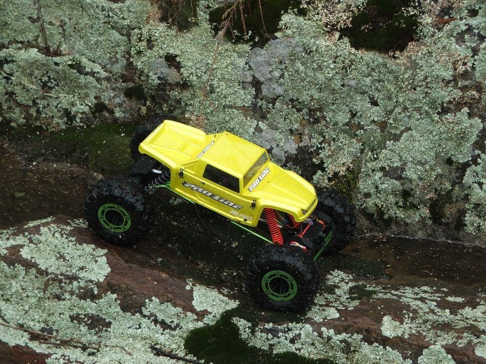 Yellow remote control rock crawler with large tires on mossy rocks