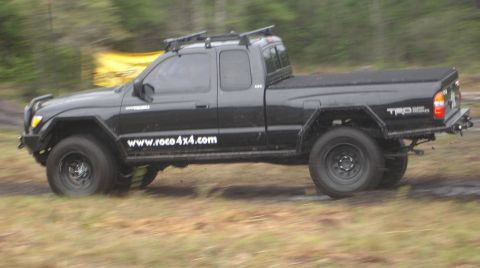 1989 Ford Bronco - This black Toyota Tacoma pickup truck is captured in motion, displaying its off-road modifications and website address.