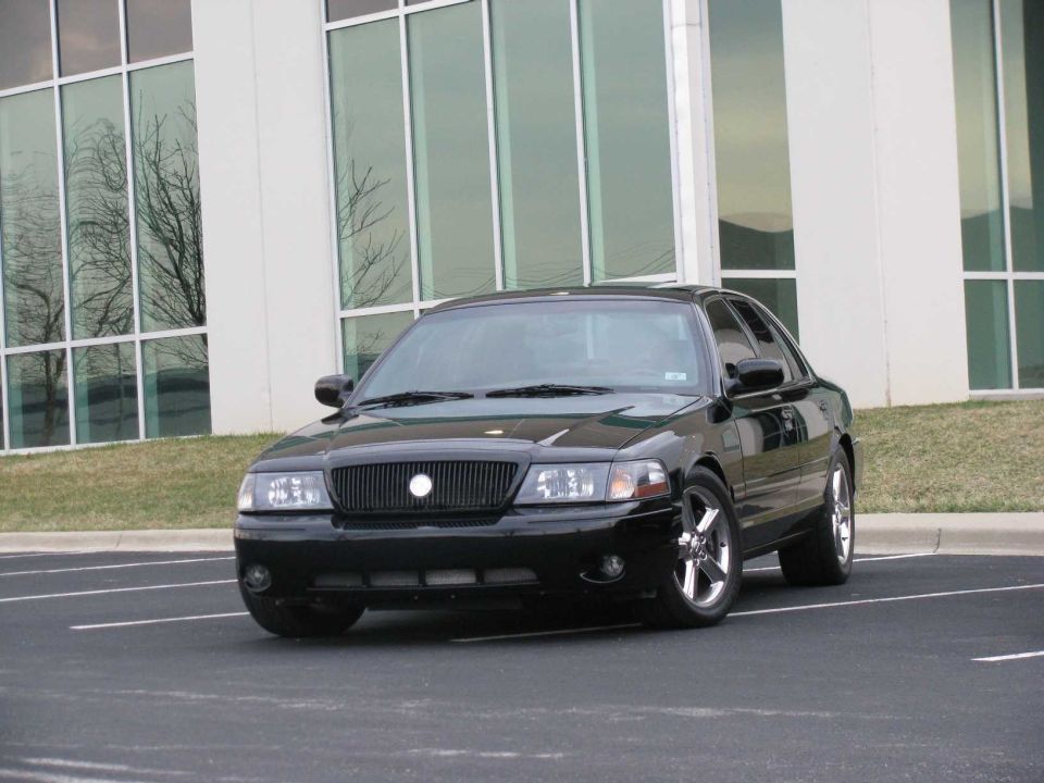Black Mercury Marauder sedan parked in a lot, front three-quarter view, glass office building behind