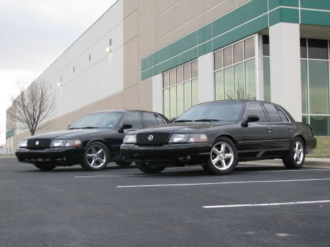 2003 Mercury Marauder - Two black sedans are parked side-by-side in front of a modern building.