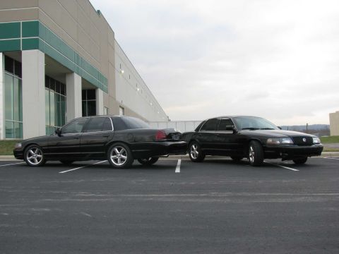 2003 Mercury Marauder - Two black 2003 Mercury Marauders are parked in a lot in front of a modern building.