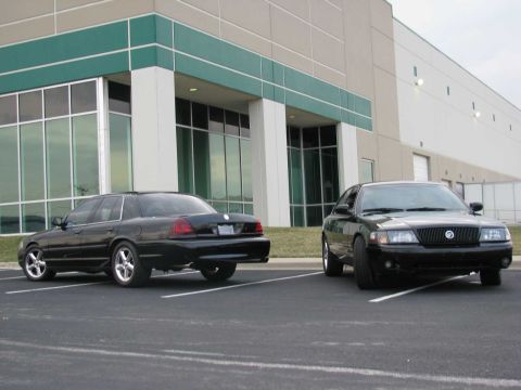 2003 Mercury Marauder - Two black Mercury Marauders are parked in front of a modern building, one facing forward and the other angled away.