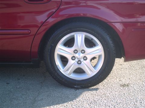 2000 Ford Taurus - The rear wheel and fender of a red sedan are visible, showing a five-spoke alloy rim.