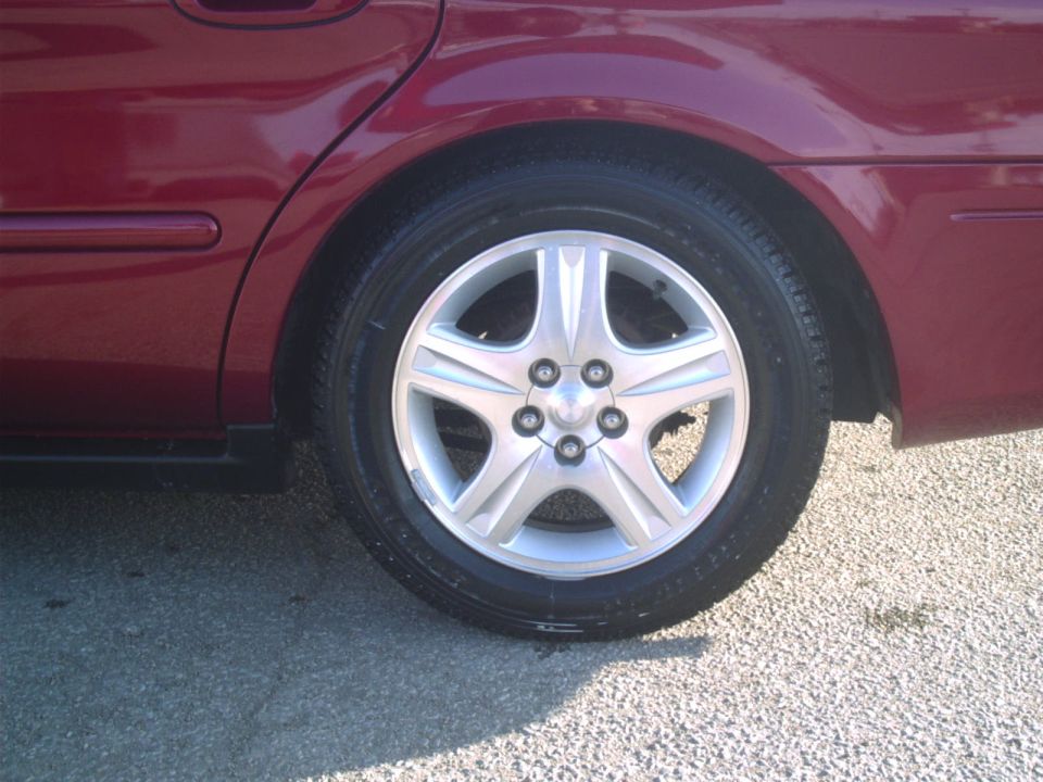 Red sedan's rear wheel with a five-spoke silver alloy rim and a portion of the fender