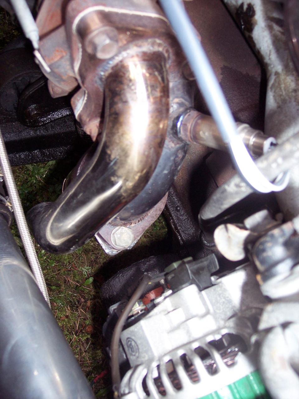 Engine exhaust manifold with shiny pipes and an alternator. Some wiring is visible