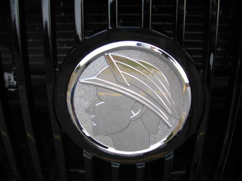 Chrome and frosted grille emblem depicting a winged helmet head, set in a black vehicle grille