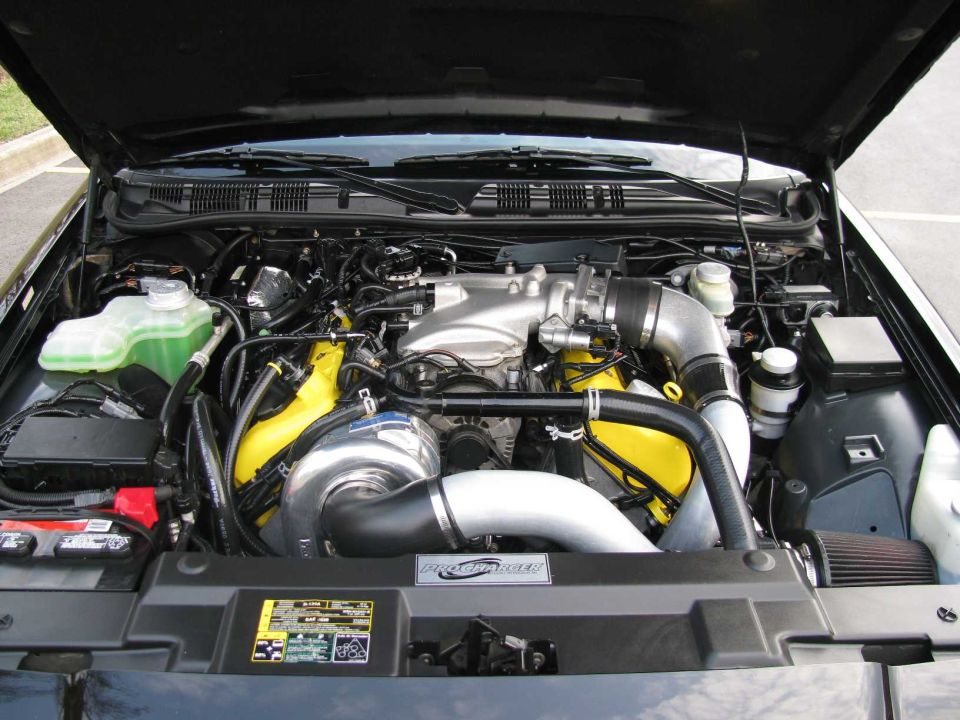 Engine bay of black sedan with ProCharger supercharger, yellow valve covers, and cone air filter