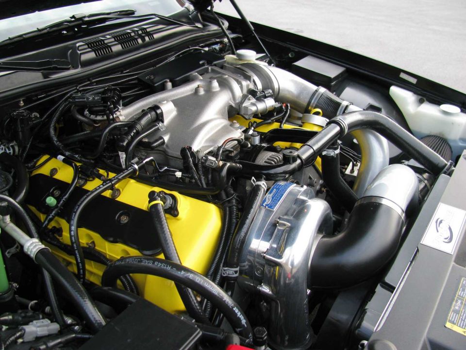 V8 engine bay with yellow coil covers, polished centrifugal supercharger and black intake tubing