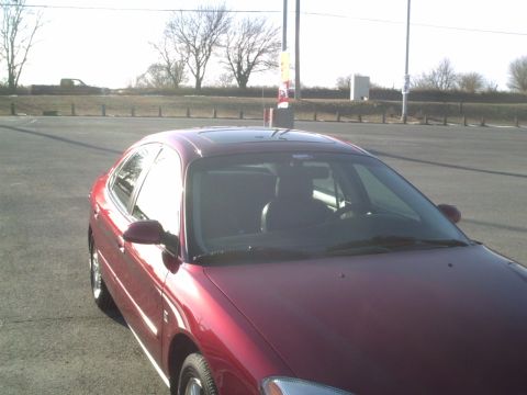 2000 Ford Taurus - A red sedan is parked outside on a sunny day. The vehicle has a sunroof and is facing towards the viewer.