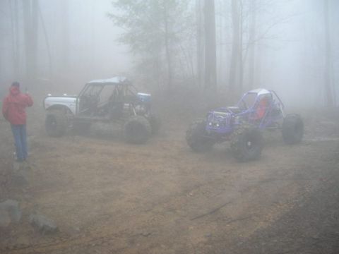 1992 Ford Mustang - Two custom off-road buggies are parked on a dirt path surrounded by trees in a dense fog.