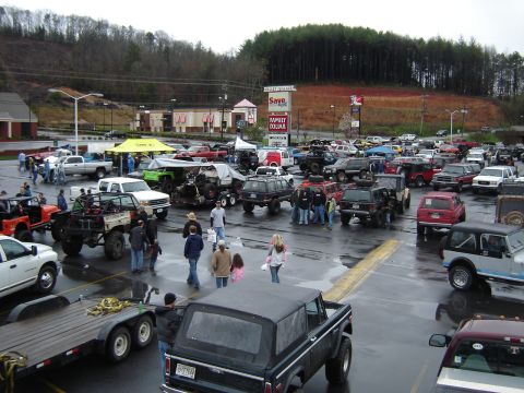 1992 Ford Mustang - A gathering of off-road vehicles in a parking lot on a cloudy day.
