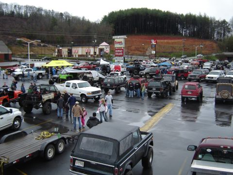 1992 Ford Mustang - A gathering of off-road vehicles in a parking lot on a cloudy day.