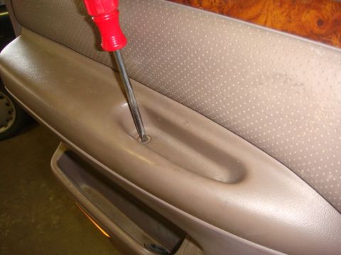 1996 Ford Bronco - Removing a screw from a vehicle's interior door panel with a screwdriver.