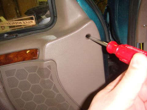1996 Ford Bronco - A screwdriver is used to remove a screw from the interior door panel of a vehicle.