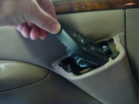 1996 Ford Bronco - A hand is shown removing a piece of black plastic trim from a car's interior door panel.