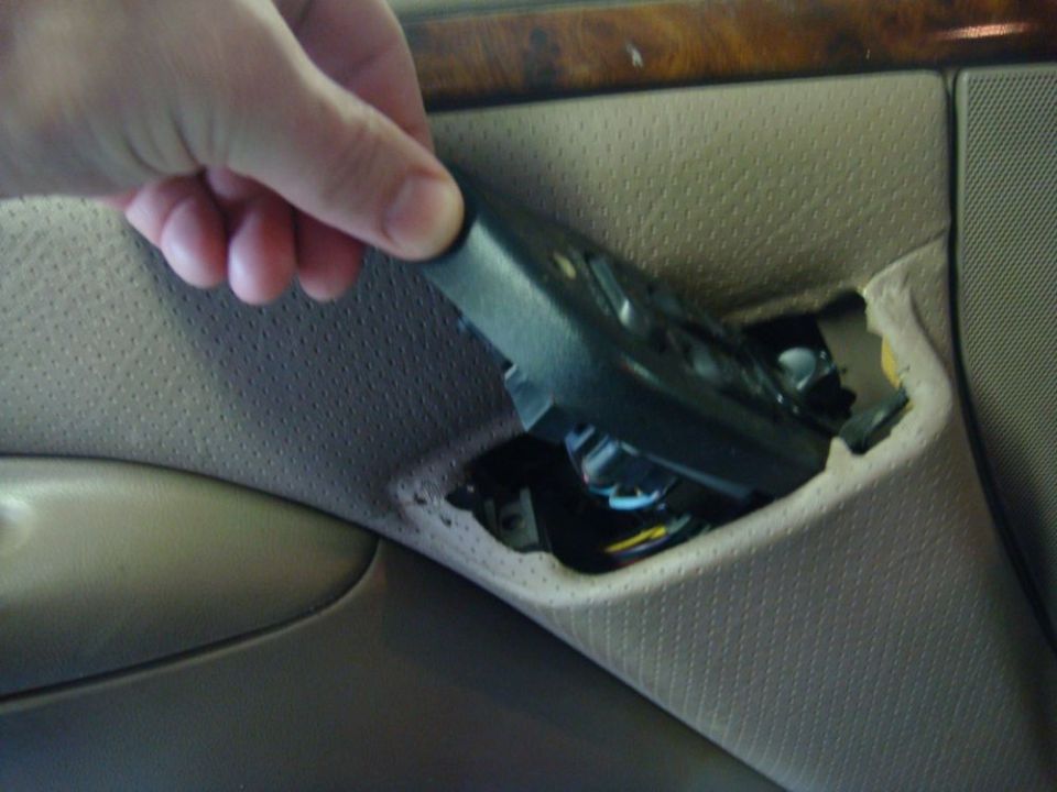 Hand removing black plastic trim from beige car door panel, exposing wires