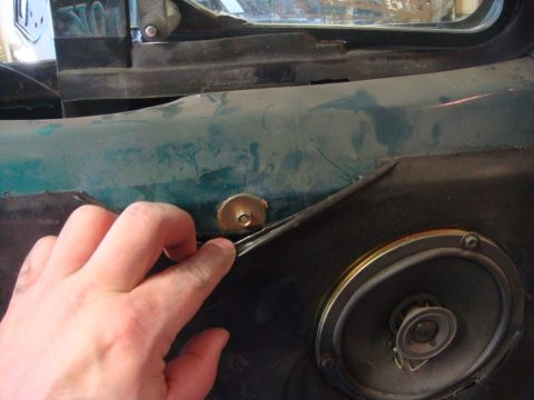 1996 Ford Bronco - Close-up of a hand removing trim from a vehicle's interior door panel, revealing a speaker.