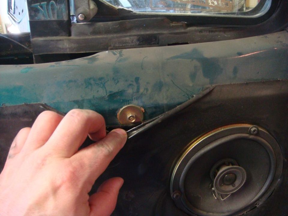 hand pulling trim off a dark interior door panel near a speaker