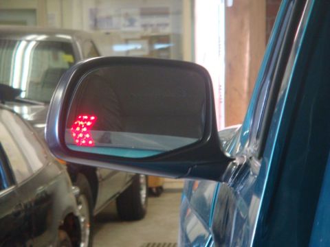 1996 Ford Bronco - A side mirror displays a red arrow indicator light, with another vehicle visible in the background.