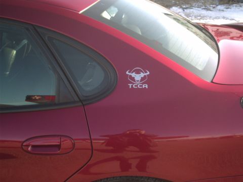 2000 Ford Taurus - A close-up of a red sedan's rear side panel shows a TCCA logo with a bull's head.