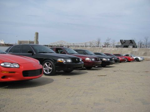 2003 Mercury Marauder - A collection of cars are lined up outdoors with a city skyline and bridge visible in the distance.