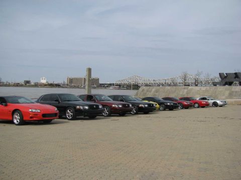 2003 Mercury Marauder - Several cars are parked in a line on a paved area near a waterfront with a bridge in the background.