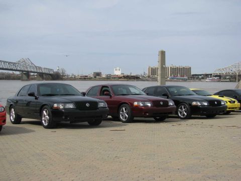 2003 Mercury Marauder - Several Mercury Marauders and a Ford Mustang are parked in a row near a waterfront.